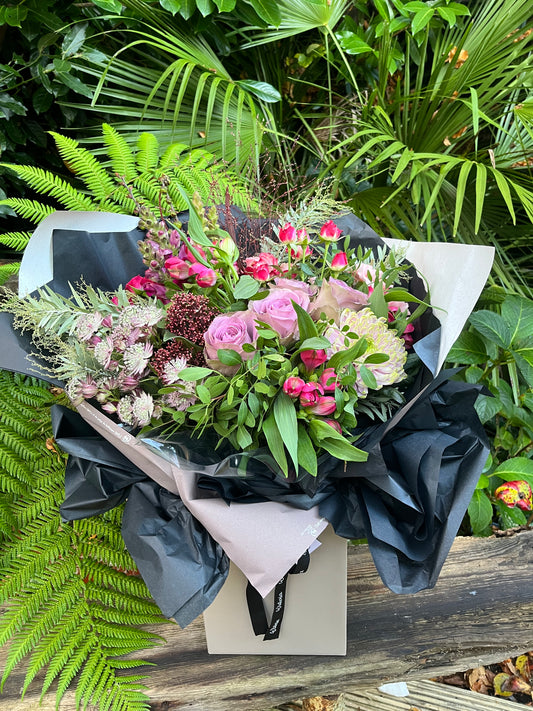 Crimson Twilight Bouquet featuring deep red, pink, and purple blooms with wild greenery, hand-tied in a dramatic and romantic style